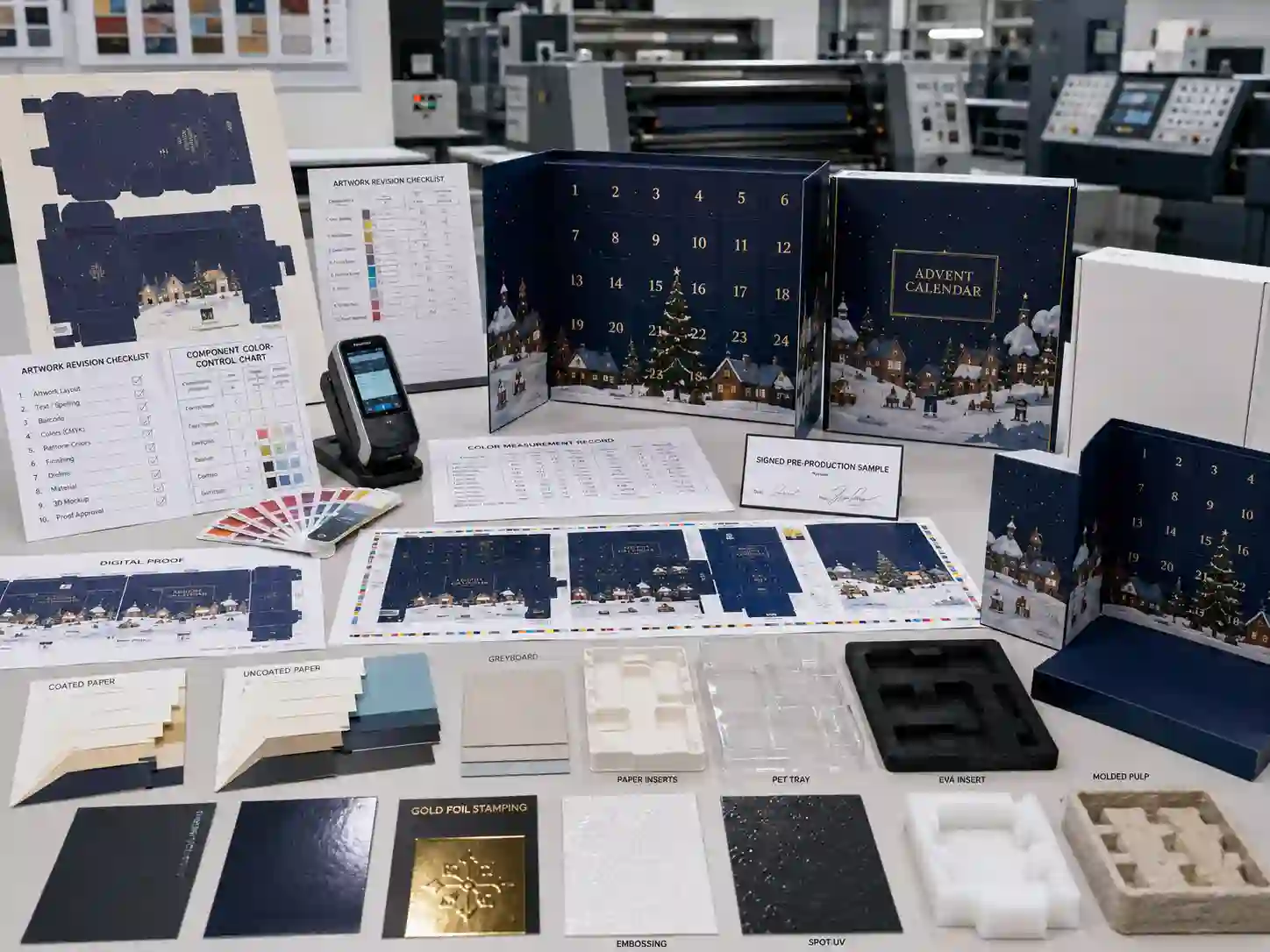 Packaging development table with color proofs, materials, dielines, and advent calendar box samples
