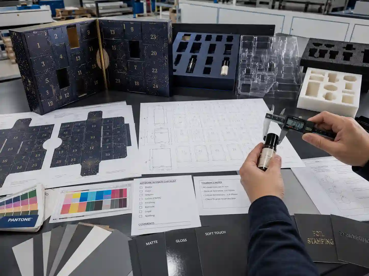 Packaging development table with product measurements, insert materials, dielines, color proofs, and finishing samples for an advent calendar