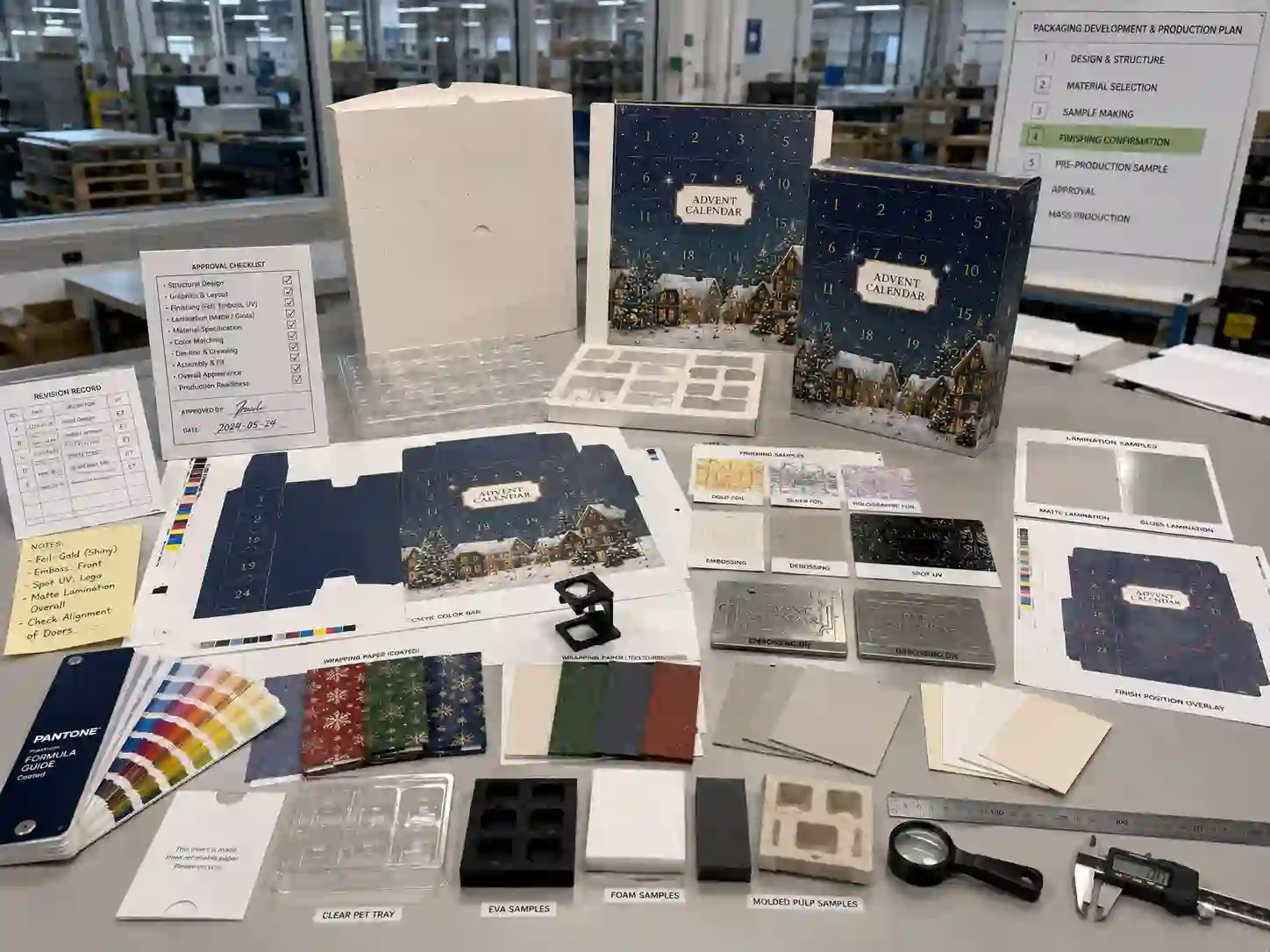 Factory sample review table with dielines, material swatches, foil tests, lamination sheets, and finishing approval documents
