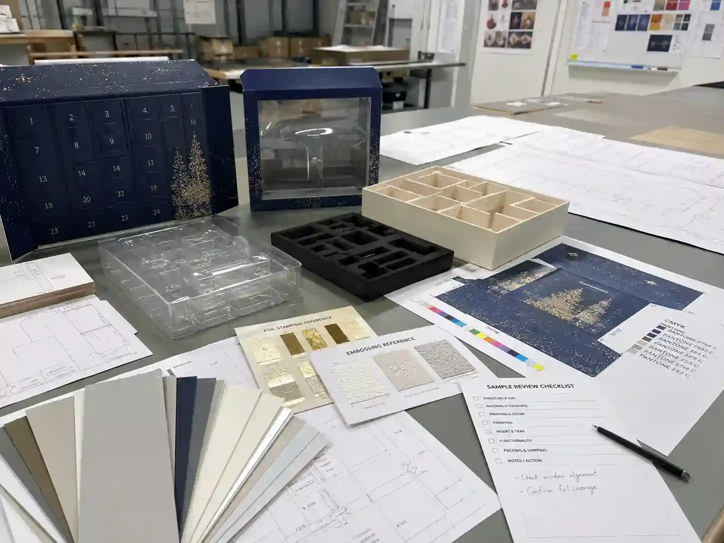 Factory planning table for makeup advent calendar boxes with dielines, material swatches, insert samples, and artwork proof