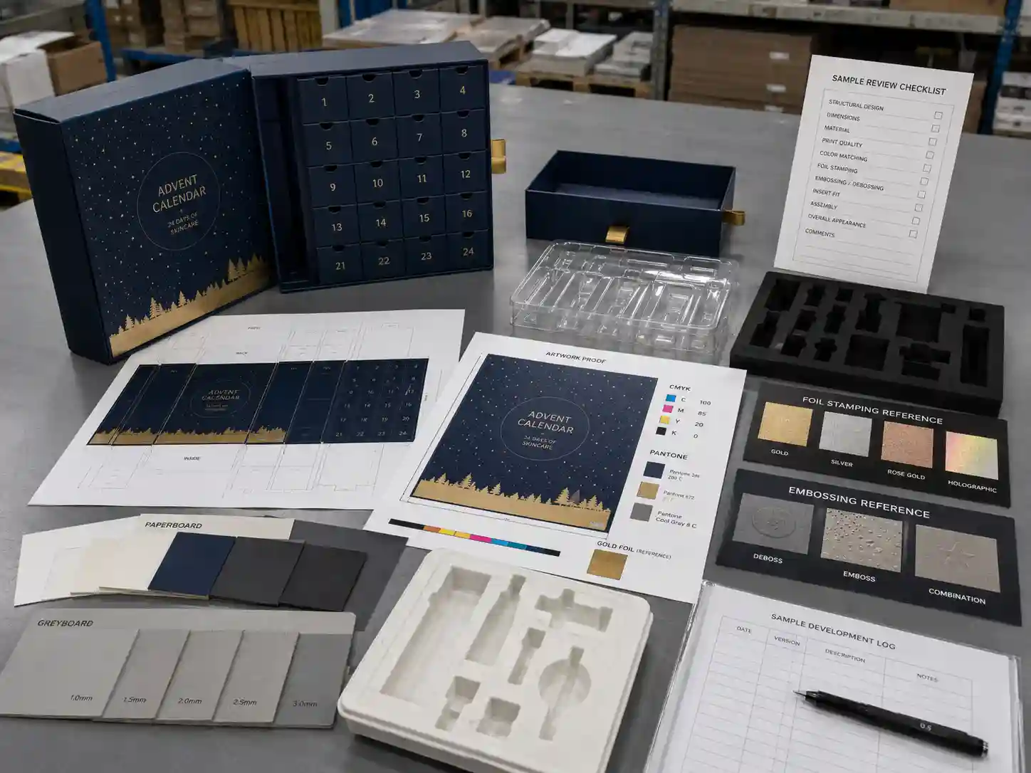 Factory planning table with dielines, material swatches, insert samples, artwork proof, and print finish references for skincare advent calendar boxes