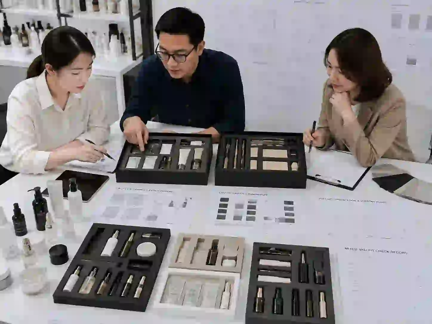 Packaging specialists reviewing sachet sample compartment presentation with beauty product samples and insert designs.